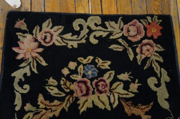 Close-up of a black rug featuring pink, red, and blue floral motifs with olive green leaves, by rugs on net. By rugs on net