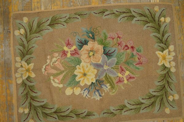 A close-up of a floral hooked rug with pastel flowers on a tan background, bordered by green leaves, by rugs on net. By rugs on net