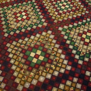 Close-up of a colorful geometric rug with checkerboard squares in reds, greens, and earth tones by Rugs On Net