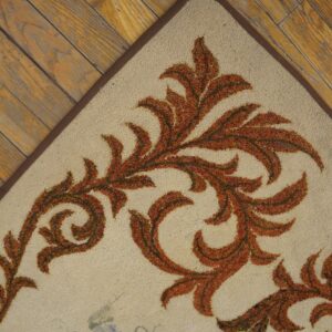 Close-up corner view of an ivory rug with burnt orange scrollwork pattern on rustic wood floor by Rugs On Net