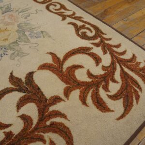 Close-up of a beige rug with rust-colored scrollwork border and faint floral details on a wooden floor by Rugs On Net