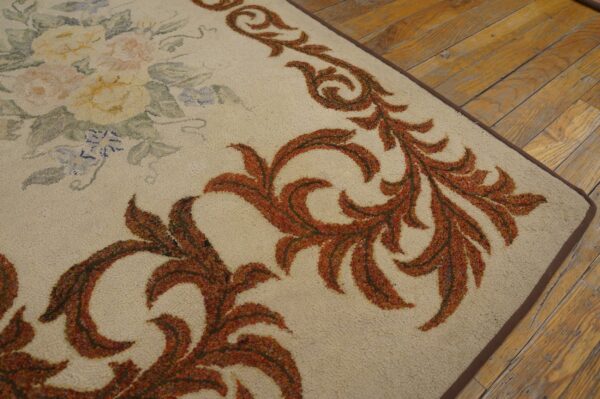Close-up of a beige rug with rust-colored scrollwork border and faint floral details on a wooden floor by rugs on net