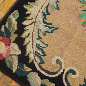 Close-up of a floral hooked rug with pink and green elements on a tan field and black border, by Rugs On Net