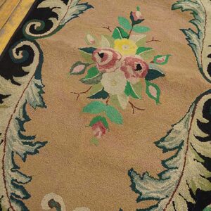 Close-up of a hooked rug featuring a central bouquet of pink and yellow roses against a tan ground, framed by black borders and scrolling foliage designs, by Rugs On Net