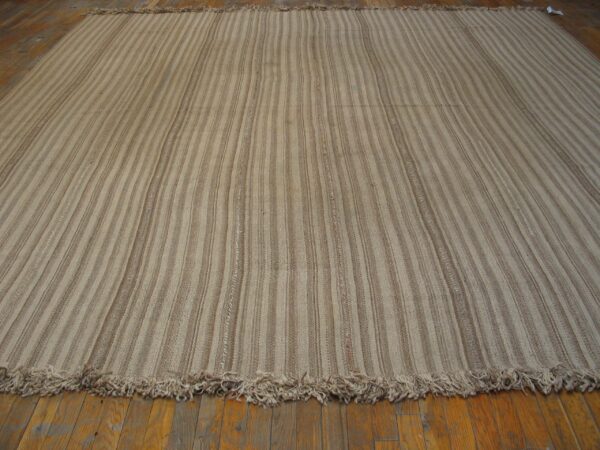Close-up of a striped beige and brown kilim rug laid on wood flooring by rugs on net. By rugs on net
