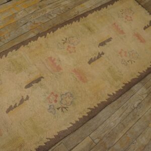 Close-up of a beige hooked rug with faint floral and abstract motifs and a scalloped brown border, placed on a rustic wooden floor by Rugs On Net. by Rugs On Net