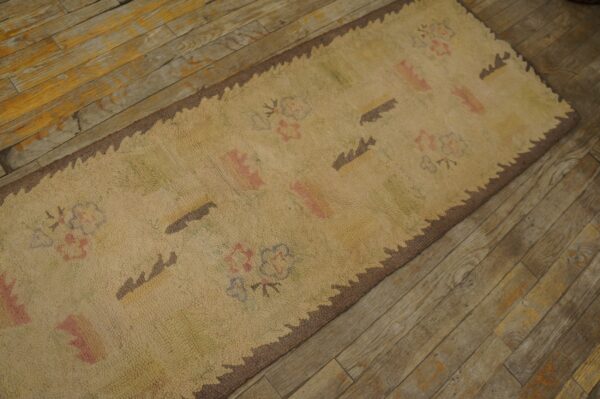 Close-up of a beige hooked rug with faint floral and abstract motifs and a scalloped brown border, placed on a rustic wooden floor by rugs on net. By rugs on net