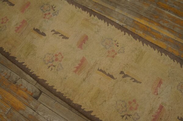 Close-up of a beige rug with subtle floral and geometric patterns, featuring a dark brown serrated border, resting on rustic wooden flooring by rugs on net. By rugs on net