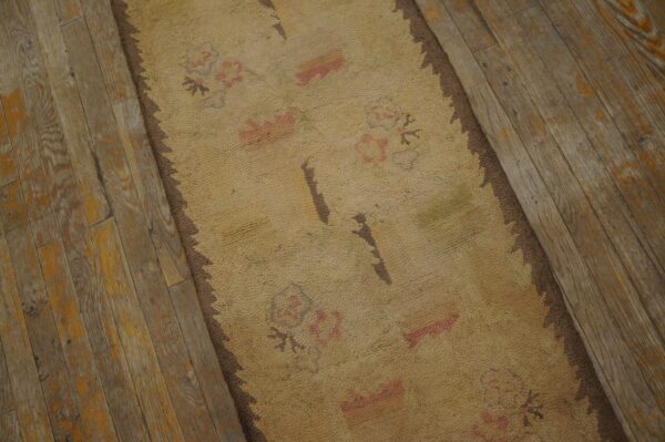 Close-up of a beige rug with faded pink floral motifs on distressed wood flooring by rugs on net. By rugs on net