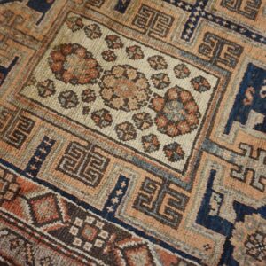Close-up of an antique rug featuring geometric and floral motifs in muted orange, blue, and cream tones, by Rugs On Net