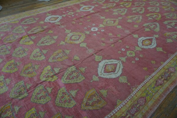 Close-up view of a faded pink rug with repeating yellow and white shield-like motifs and scattered floral elements, by rugs on net. By rugs on net