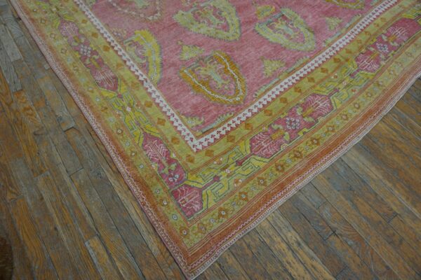 Close-up corner view of a pink and yellow patterned rug on rustic wood flooring by rugs on net. By rugs on net