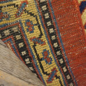 Close-up of the folded edge of an antique rug showing vibrant yellow, red, and blue geometric patterns on a wooden floor by Rugs On Net. by Rugs On Net