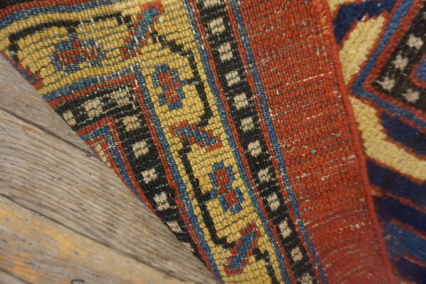 Close-up of the folded edge of an antique rug showing vibrant yellow, red, and blue geometric patterns on a wooden floor by rugs on net. By rugs on net