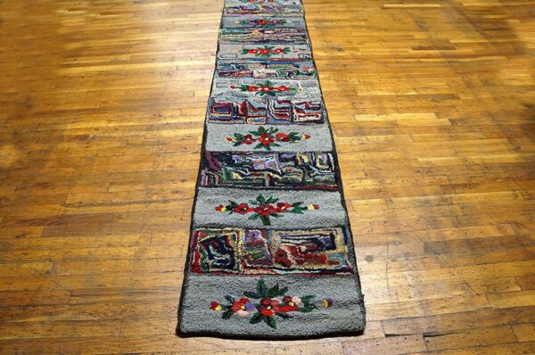 A long, narrow hooked rug with repeating floral and abstract panels on a wooden floor by rugs on net. By rugs on net