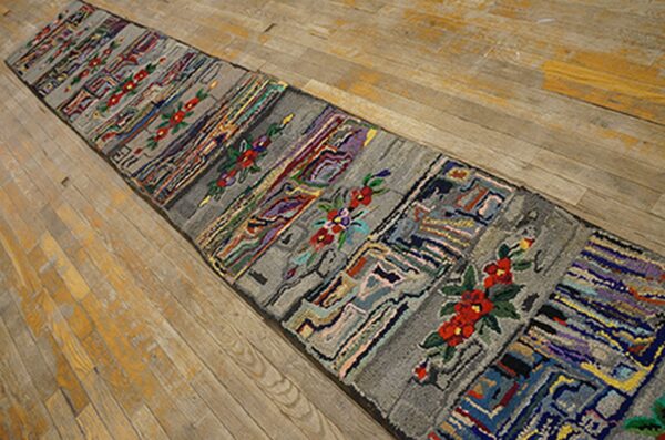 A long, narrow rag rug with gray panels interspersed with colorful abstract patterns and red floral motifs, laid on a light wooden floor by rugs on net. By rugs on net