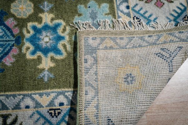 Light green beige kazak rug corner folded showing the back