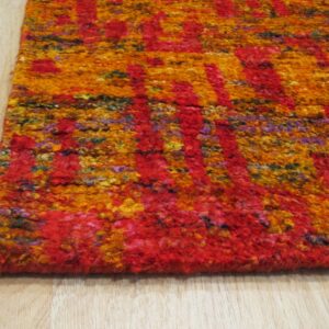 Anand red sari-silk rug corner detail showing abstract gold and orange pattern