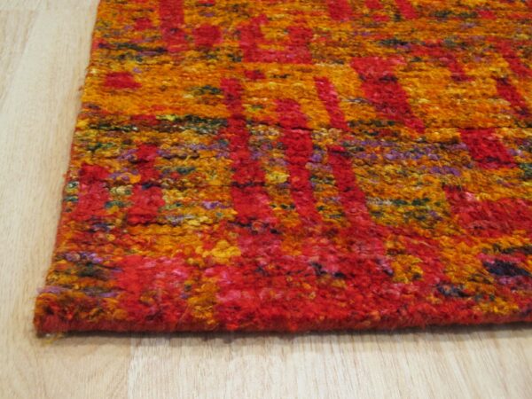 Anand red sari-silk rug corner detail showing abstract gold and orange pattern
