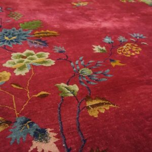 Close detail of the deep red field of a Chinese Art Deco rug with gold and olive peonies and teal foliage