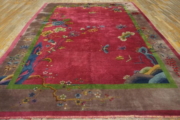 Antique red color classic chinese art deco design room size carpet 3 Angled view of a red 1920s chinese art deco carpet on a wood plank floor, showing the taupe border and blue rockwork along the lower edge