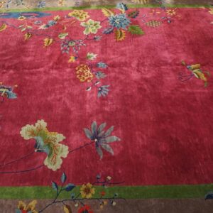 Upper corner of a red Chinese Art Deco rug with gold and cream blossoms and blue-grey leaves meeting the green frame and taupe border