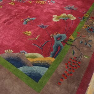 Corner detail of a red Art Deco Chinese carpet on wood flooring, with blue-green rockwork and a cluster of red berries beside the green frame