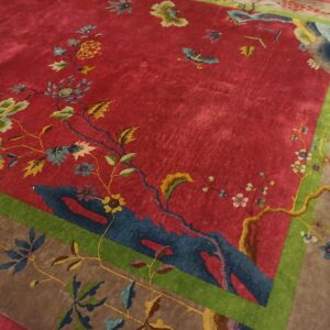 Angled corner of a red 1920s Chinese Art Deco carpet on a wood floor, with blue rockwork and gold and cream peonies