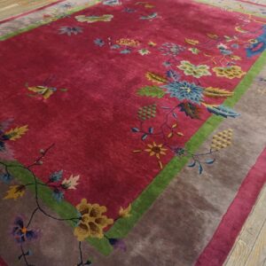 Angled full view of a red Chinese Art Deco room size rug on plank flooring, showing the green frame and taupe outer border