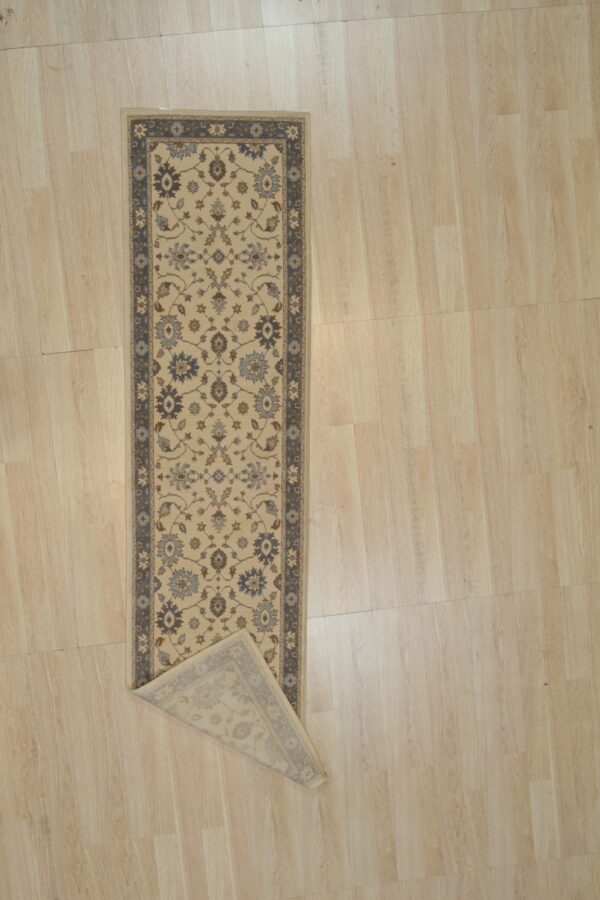 Ivory and slate blue oushak wool runner rug with a corner folded back to show the hand knotted pile and backing