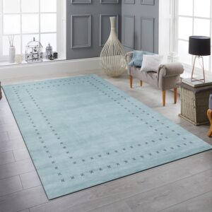 Soft aqua wool area rug with a dark cross motif border in a bright living room with a gray armchair.