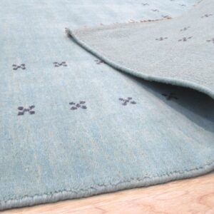 Corner of the aqua wool rug folded back to show the hand knotted foundation and low even pile.